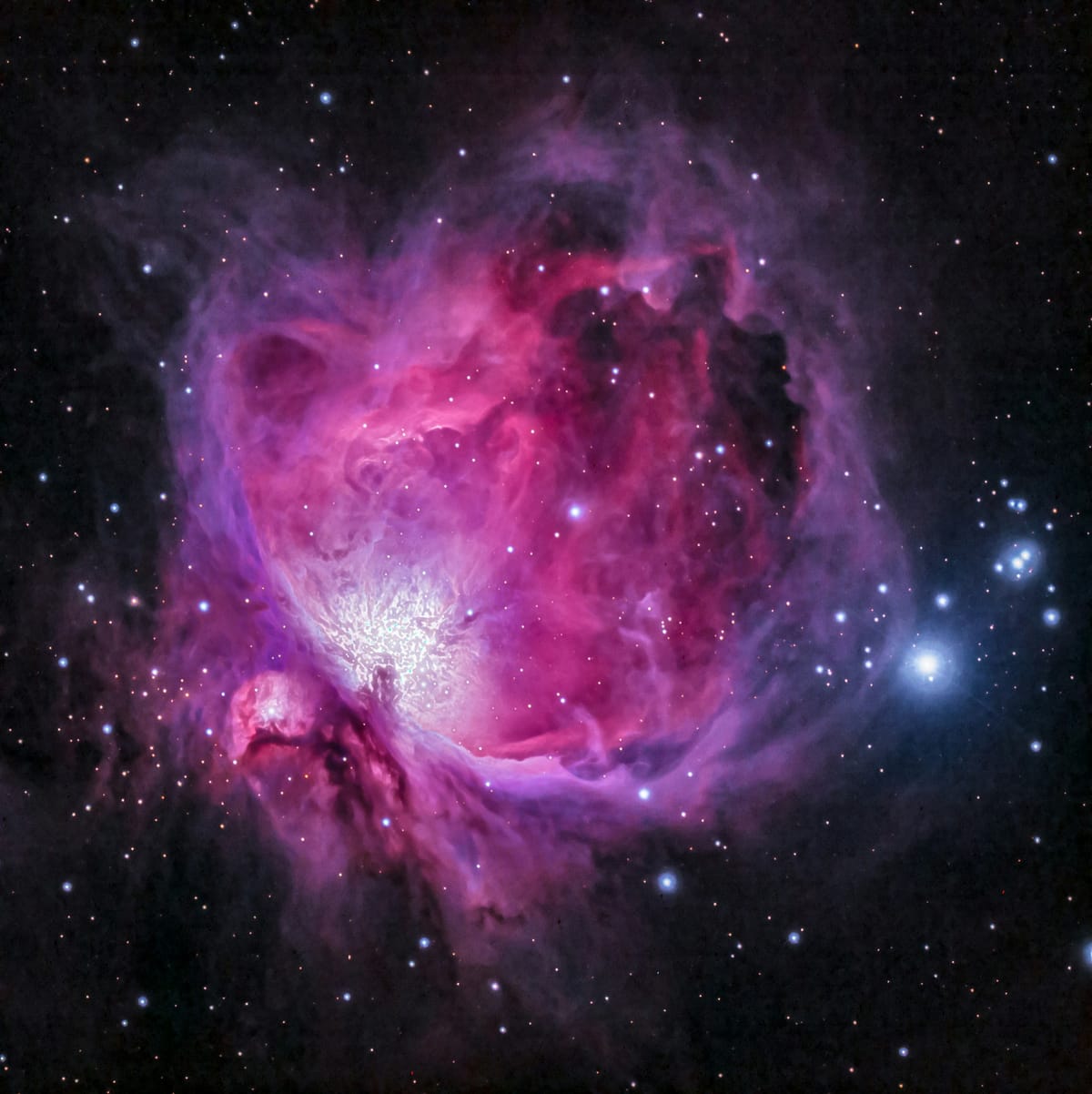 A bright hot pink and purple nebula, surrounded and dotted by blue-white & pinkish-red stars set against the ink-black space